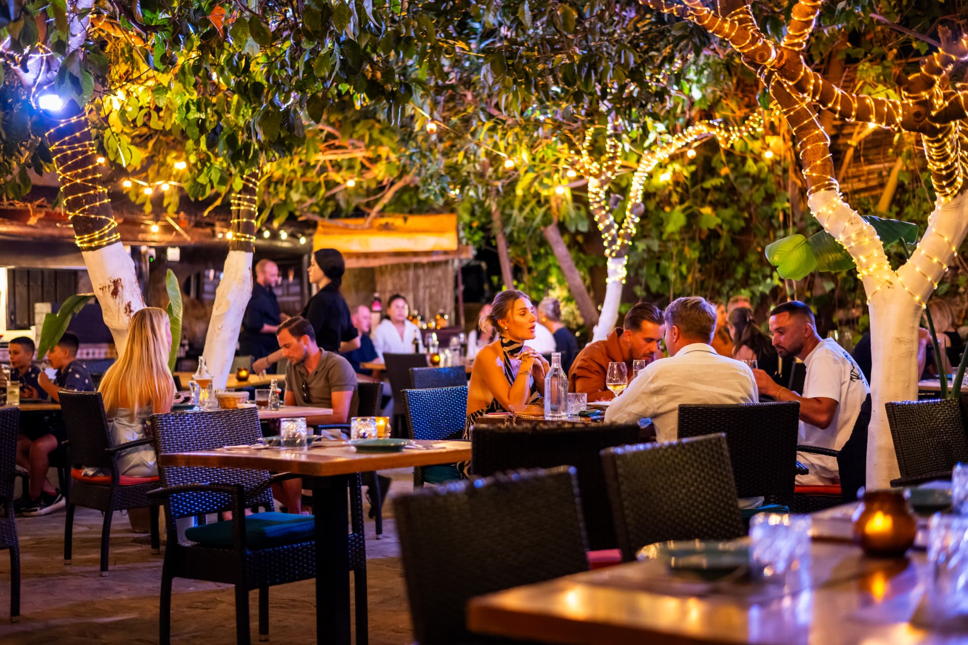 Guests dining under twinkling lights on Le Patio's outdoor terrace at night